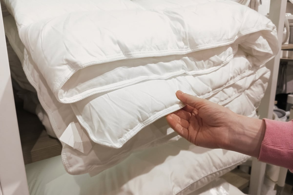 A customer's hand feeling the soft weave of a white bed blanket